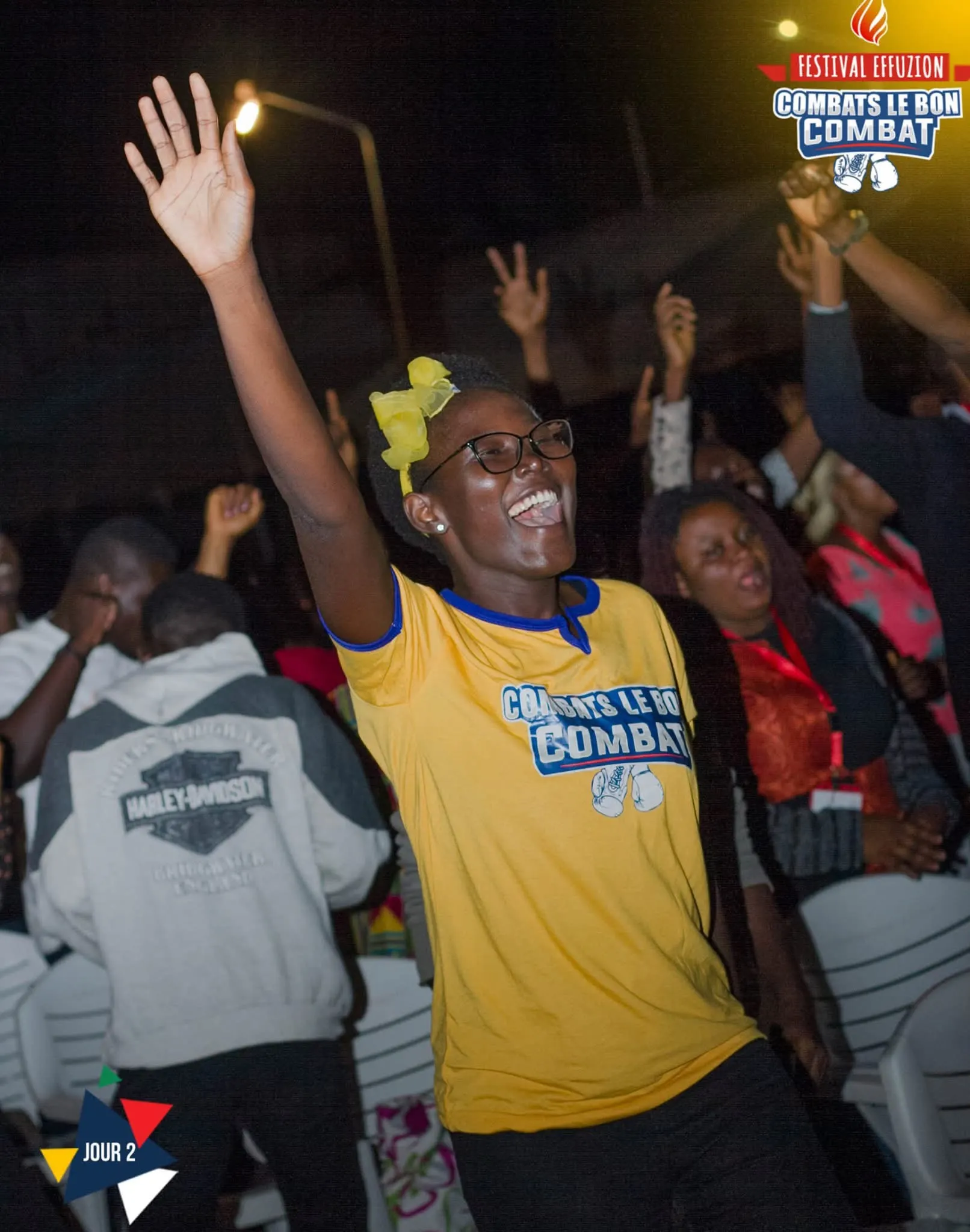 De nuit, une jeune femme en t-shirt jaune du festival lève la main en chantant. Photo de l’événement Effuzion.