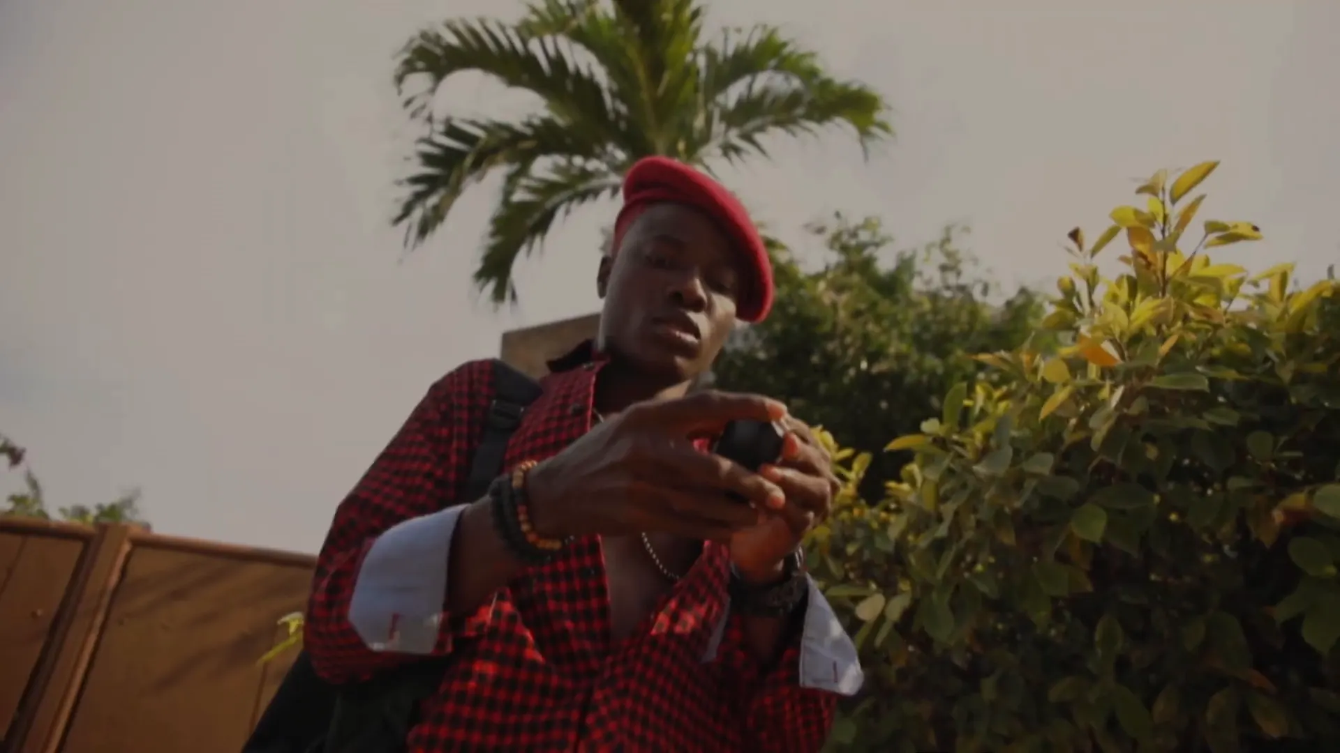 Un personnage en béret et chemise rouges dans un jardin. Image extraite du clip.