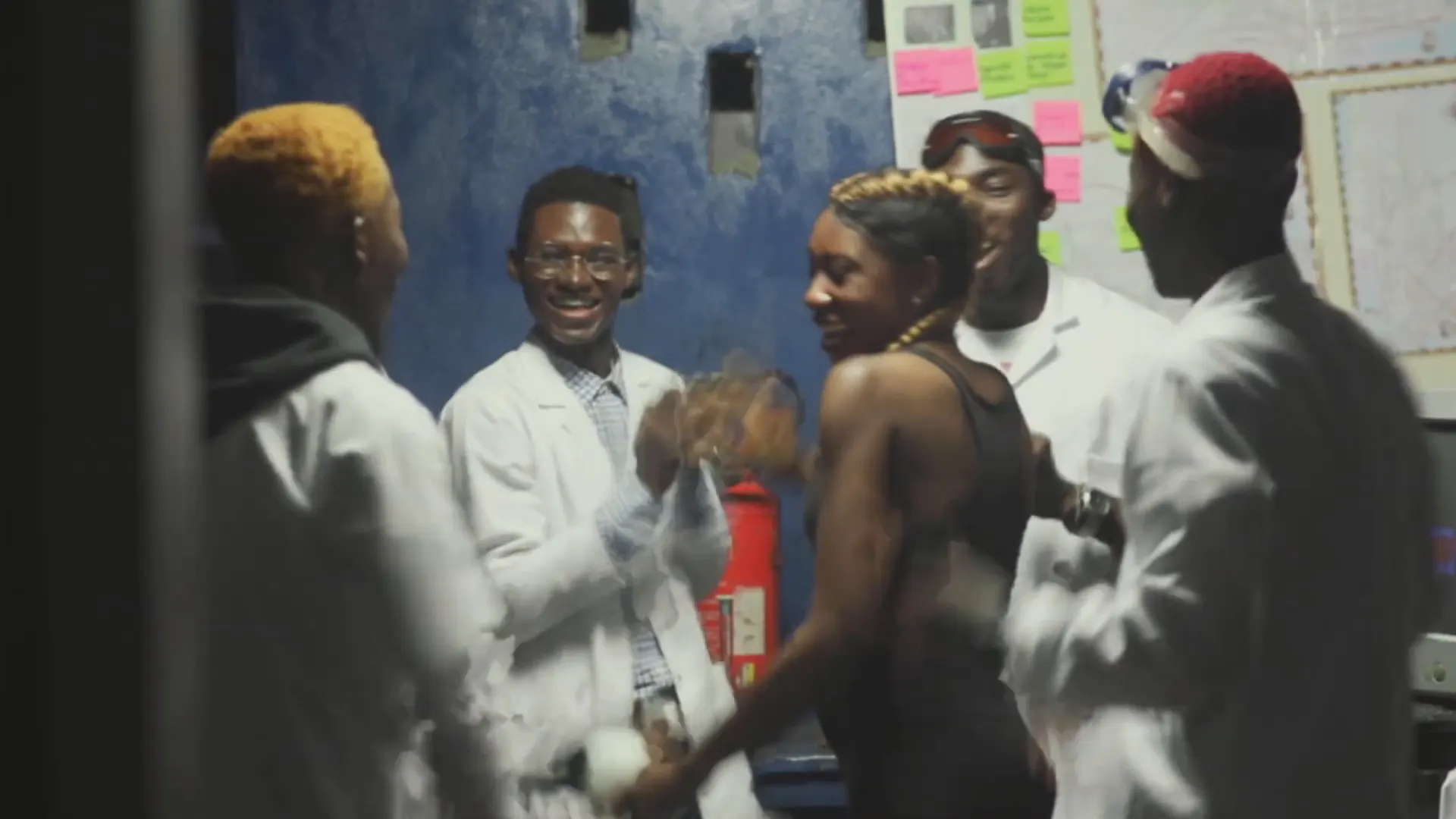 Le groupe en blouses blanches rit dans le laboratoire. Image extraite du clip.