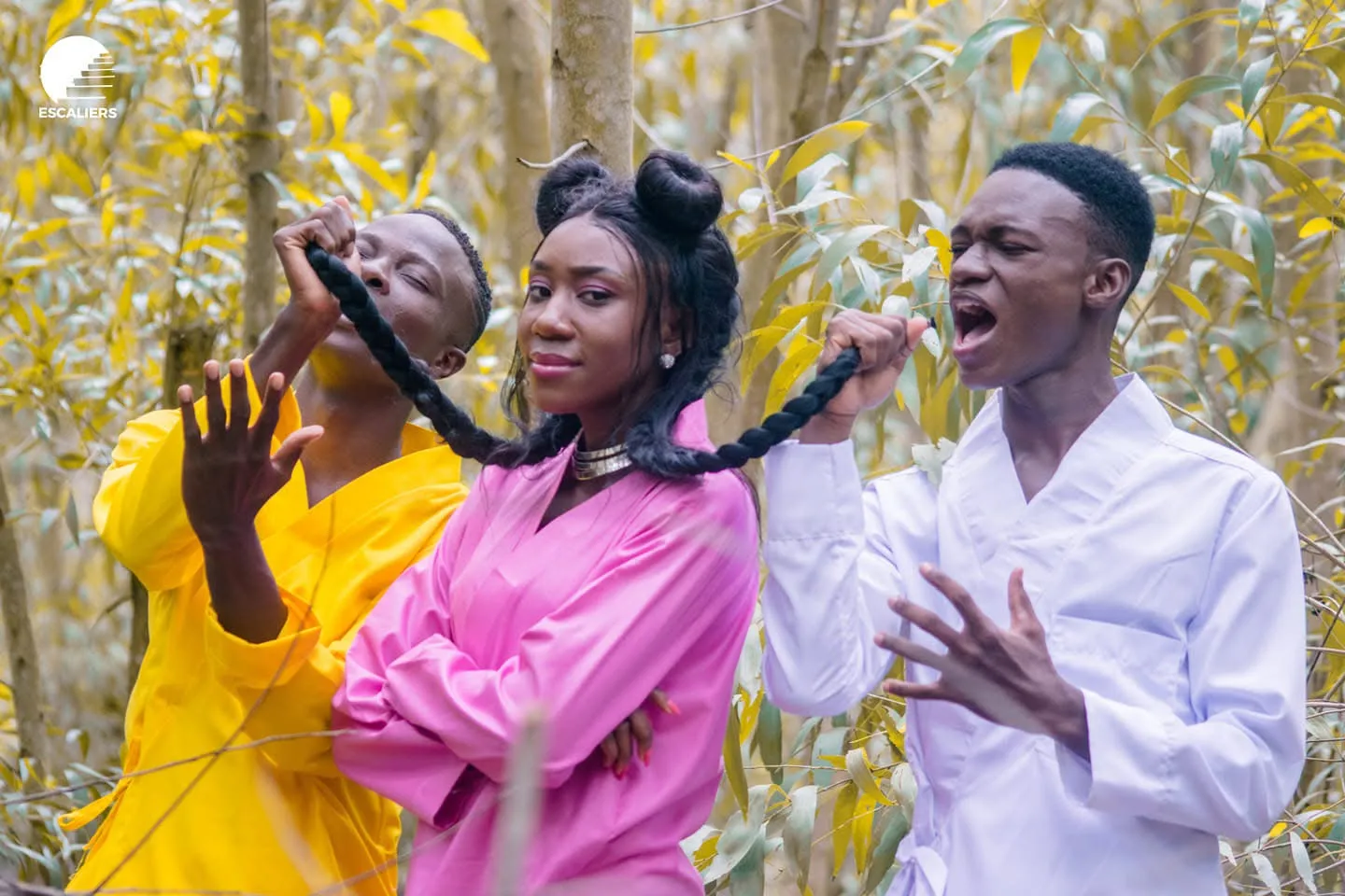 Trois chanteurs en jaune, rose et blanc jouent avec une tresse, sous les arbres. Visuel de la campagne STOP — Ma vie doit compter.