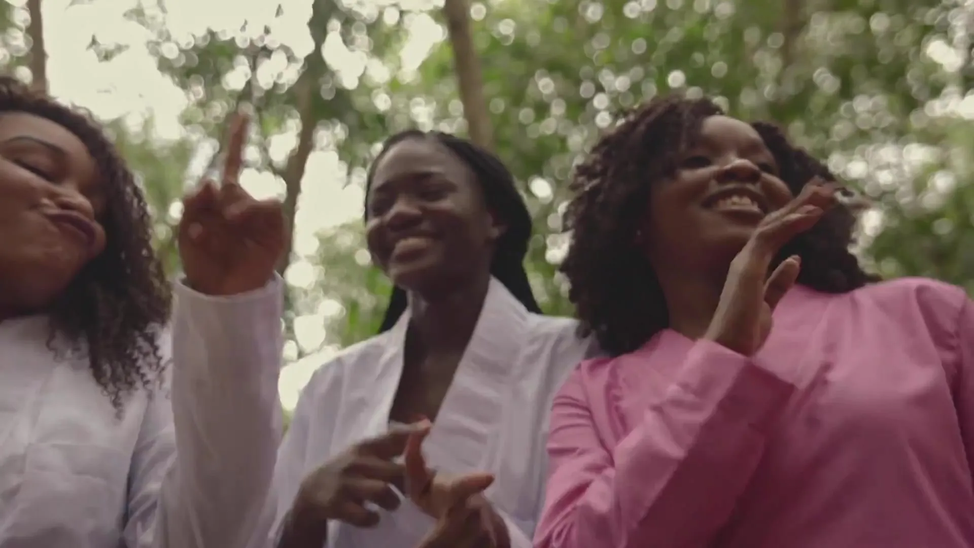 Trois chanteuses en rose et blanc, mains levées, sourires. Image extraite du clip officiel.